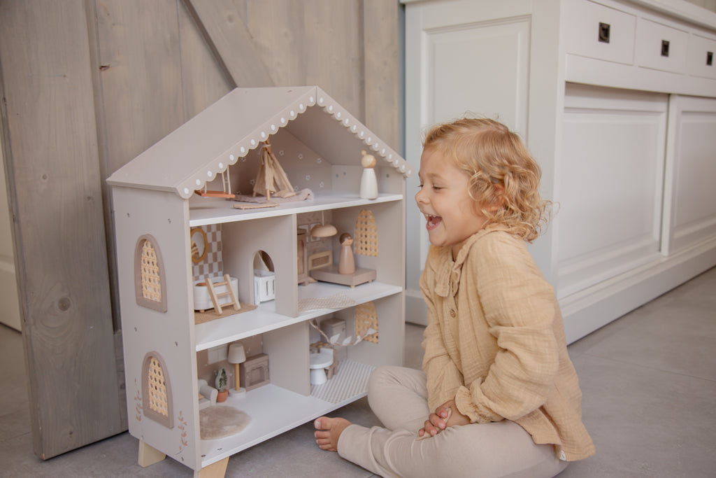 Petite fille qui joue avec la maison de poupée en bois avec mobilier et figurines enfants