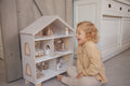 Petite fille qui joue avec la maison de poupée en bois avec mobilier et figurines enfants