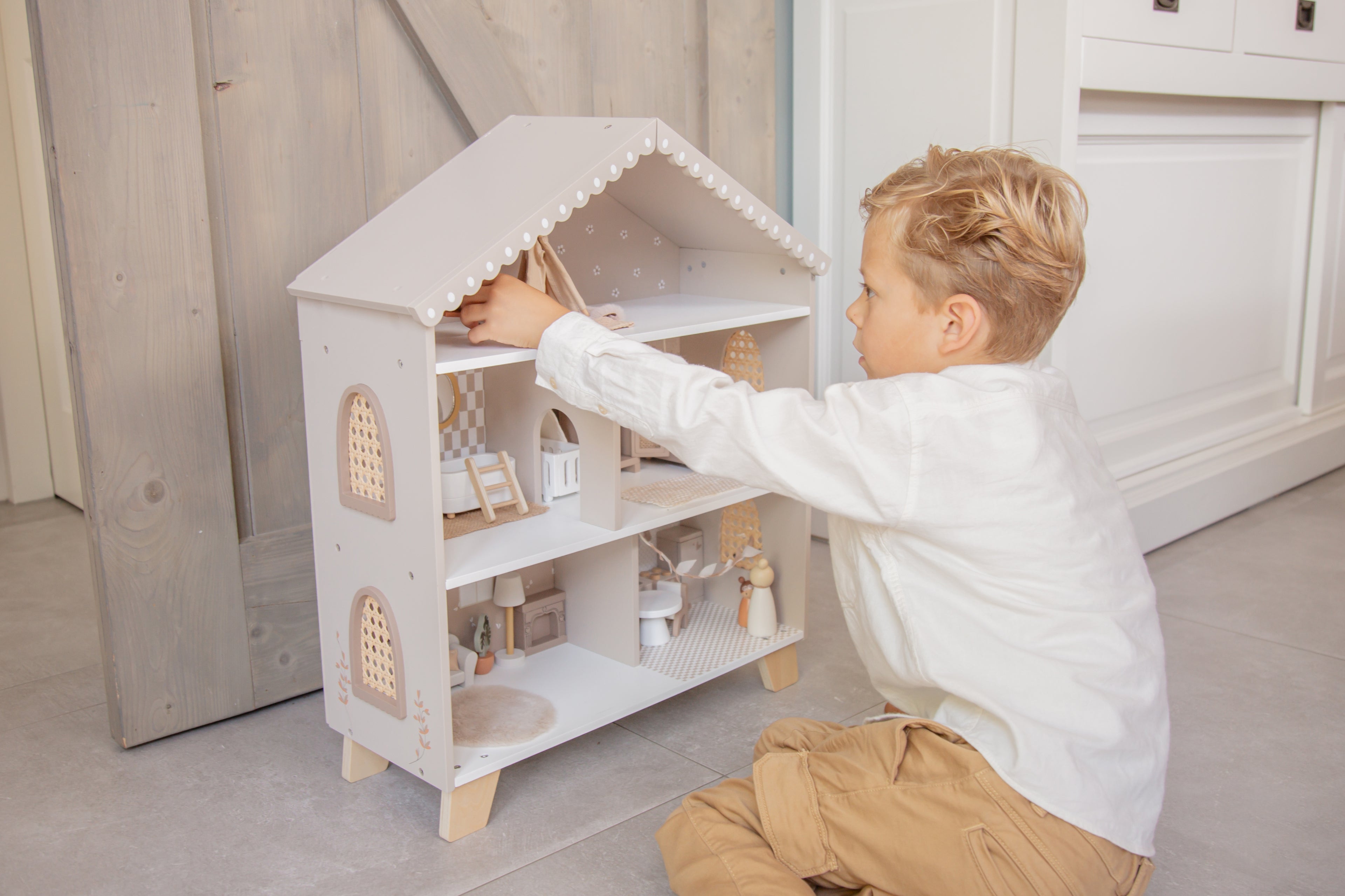 Petit garçon qui joue avec la maison de poupée en bois avec mobilier et figurines enfants